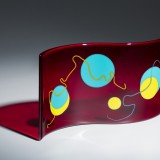 Curved red glass sculpture with colorful circles