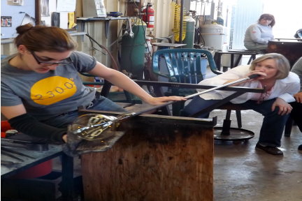 Woman glassblower shaping molten glass with instructor